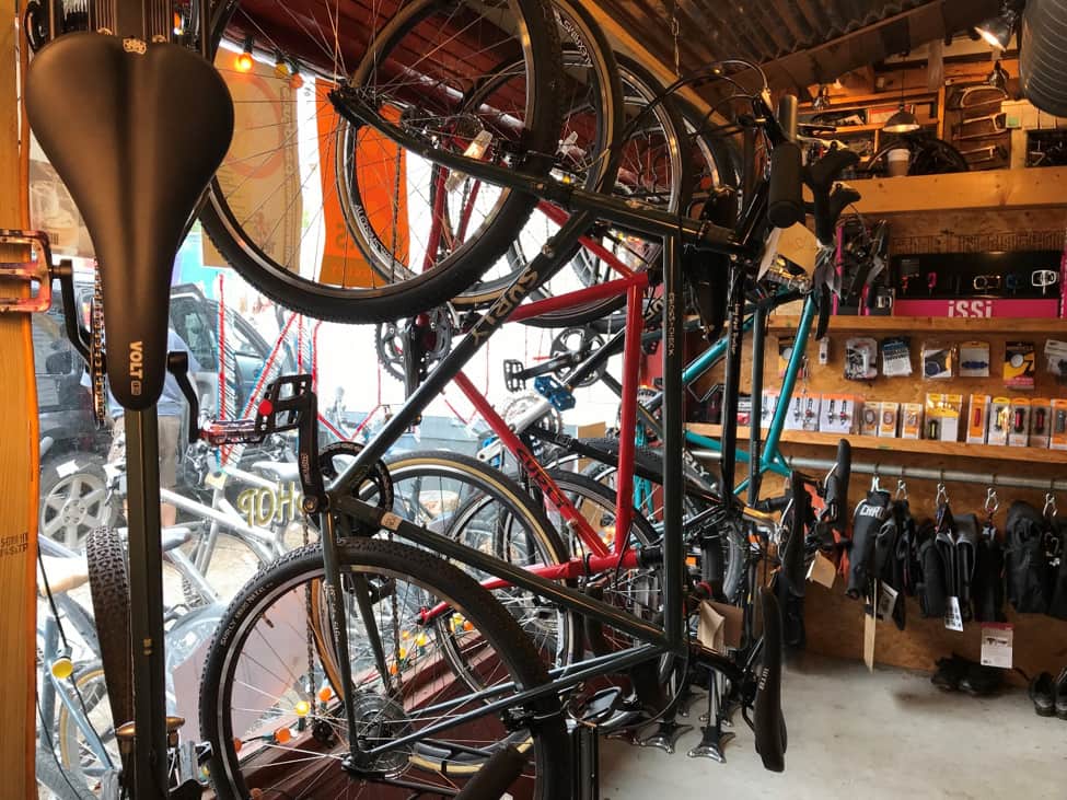 Left side view of Surly bikes hanging on a rack at the front window of a bike shop