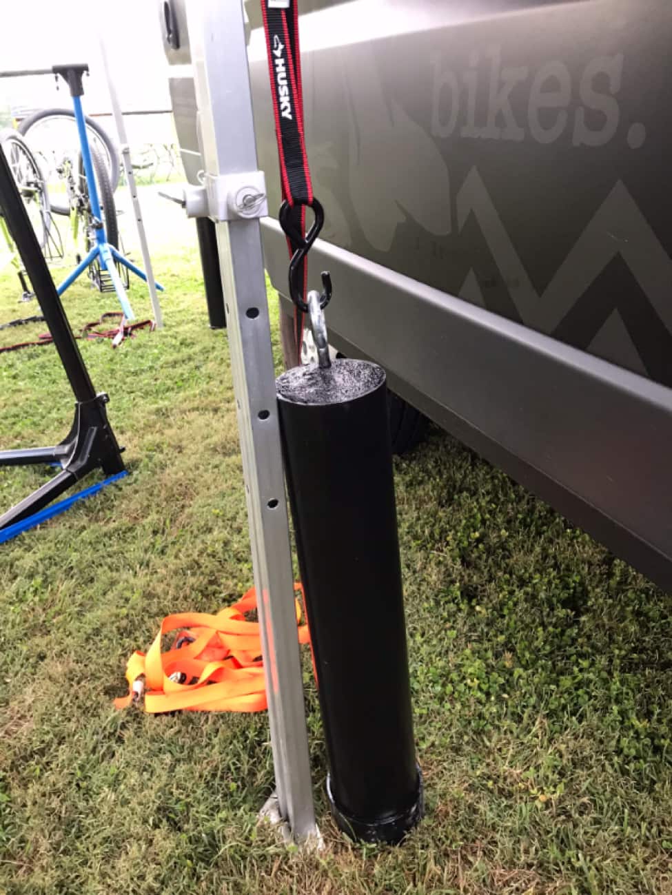An upright leg of a canopy and anchor post next to a black Surly van on grass, with bike repair stands in the background