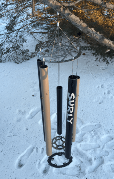 A wind chime made from Surly bike parts, on a tree branch hovering over snowy ground