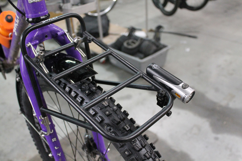 Downward view of the front end of a Karate Monkey bike, purple, with a Surly 8 Pack rack with a headlight attached