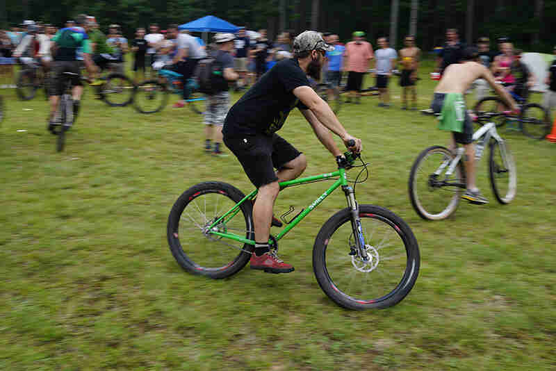 Right side view of a cyclist riding a green Surly bike in a circle on a grass field with other cyclists