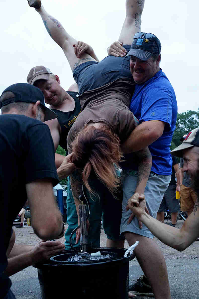 2 people hold another person doing a keg stand, while others cheer them on