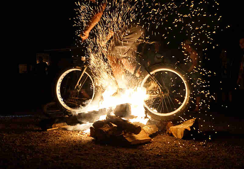 Left side view of a cyclist riding a fat bike through a campfire at night