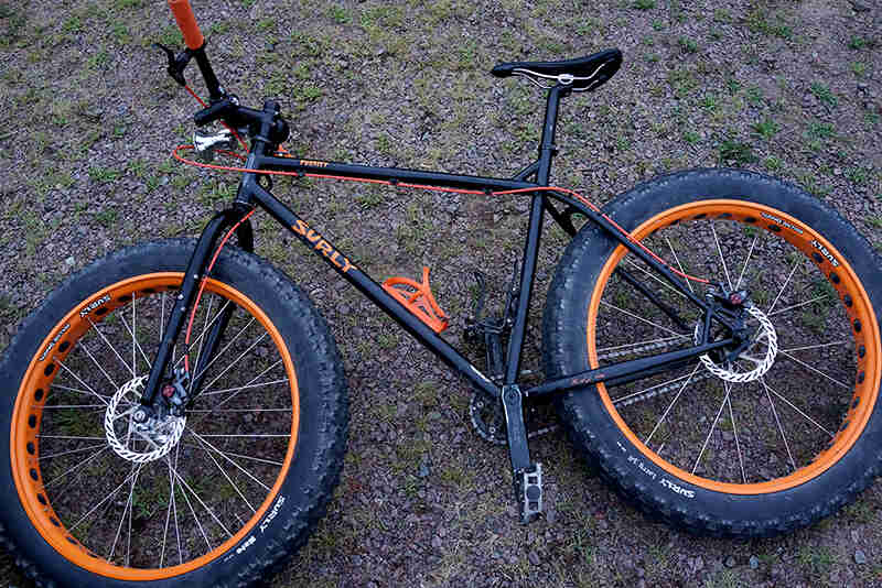 Downward view of the left side of a black and orange Surly Pugsley fat bike, laying on ground