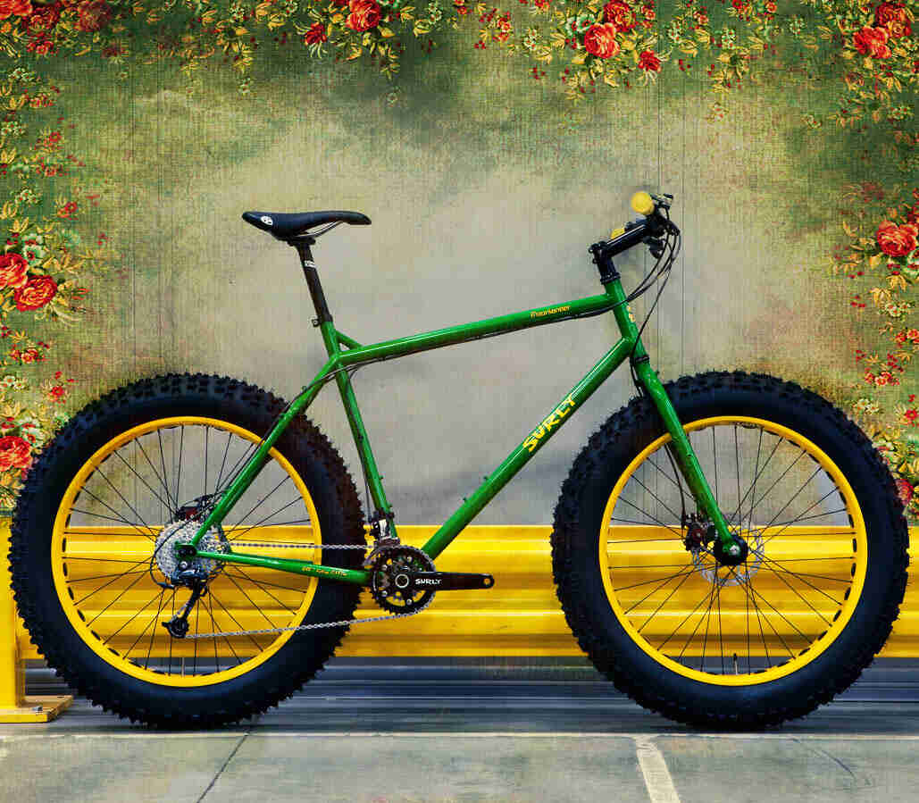 Right side view of a green Surly Moonlander fat bike with yellow rims, parked on cement along a yellow road guard