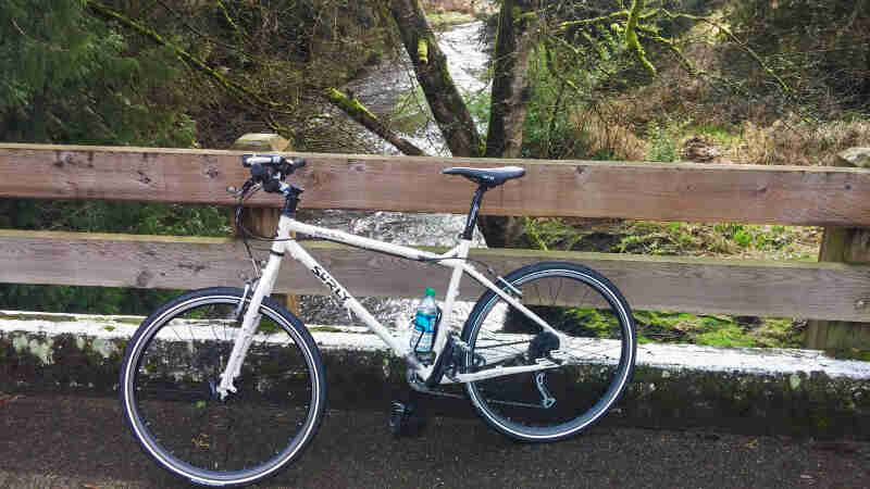 Left side view of a white Surly Troll bike, parked on a bridge over a river, along the railing