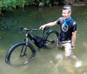 Front, left side view of a Surly bike with a frame pack, and a cyclist beside, standing in mid-thigh deep water
