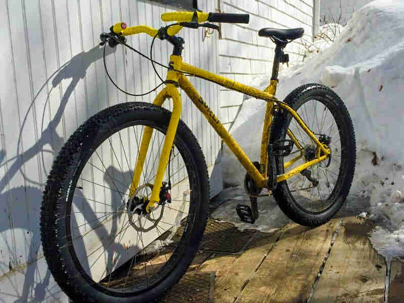 Surly Krampus bike - yellow - front left view - parked on a wood deck, leaning against a white wall