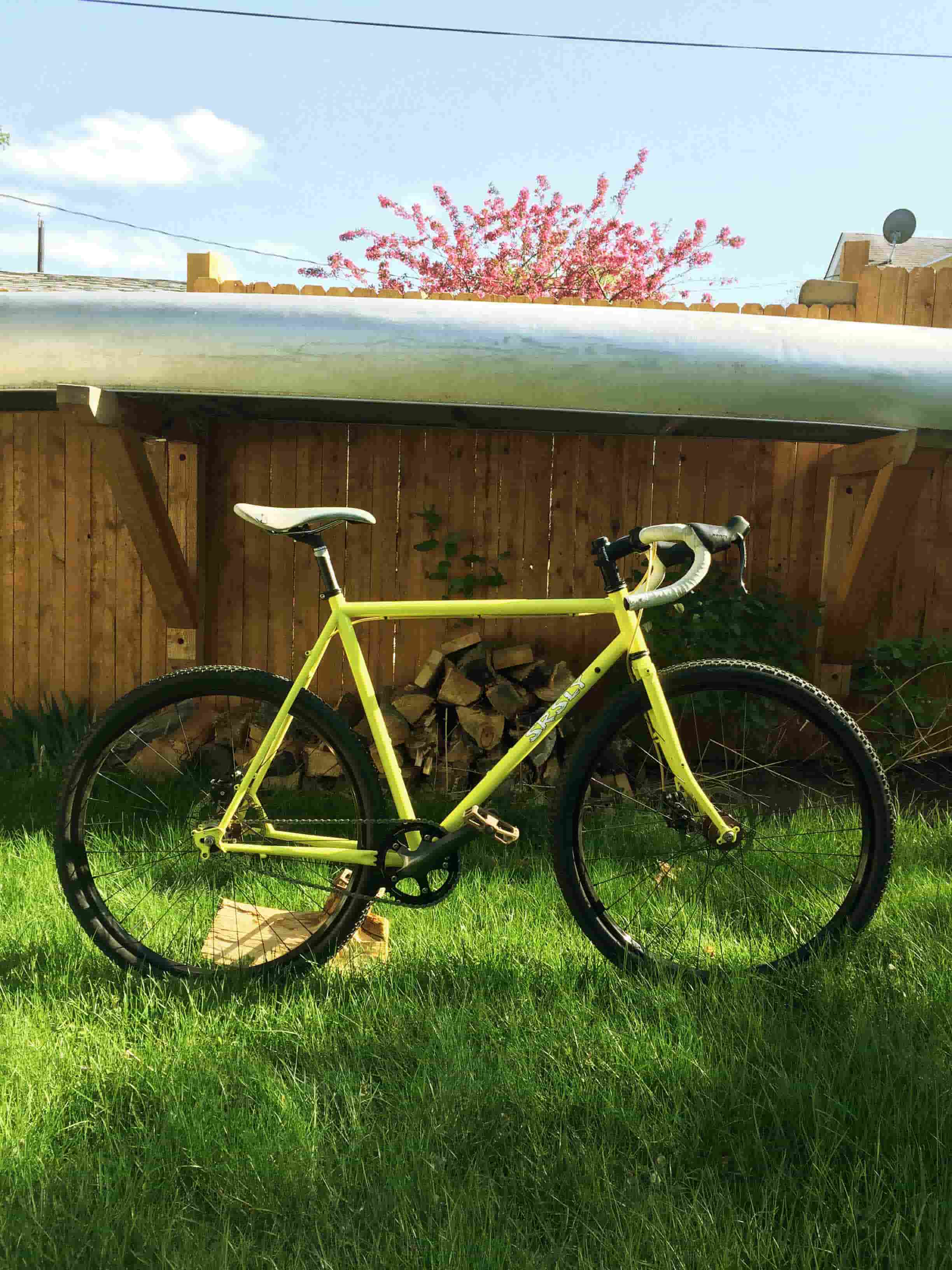 Right side view of a lime green Surly Straggler bike, parked in a grass yard, with a wood fence wall in the background