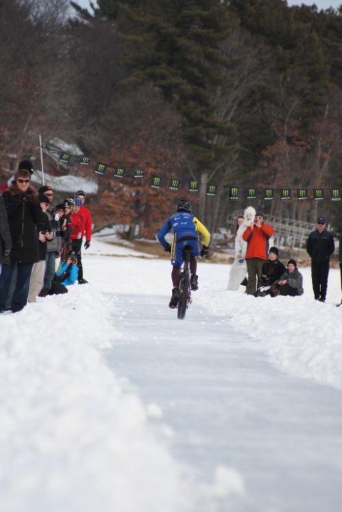 Rear view of a cyclist, riding a Surly fat bike down a cleared path on a frozen lake, with spectators on the sides