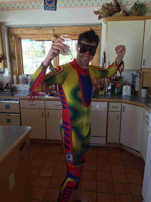 A person holding up their arms, wearing a colorful bike race suit, standing in a kitchen