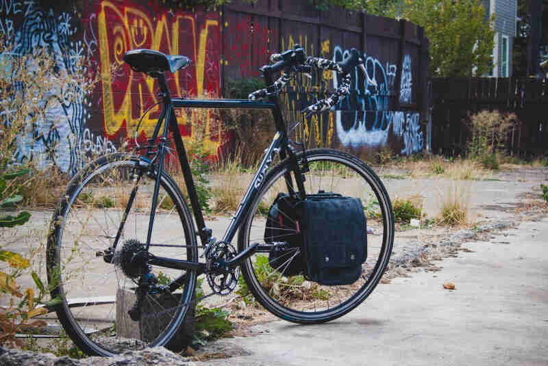 Right side view of a black Surly bike, parked on a concrete lot with weeds, and a wall covered in graffiti behind