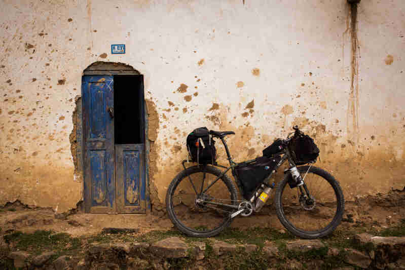 Right side view of a Surly bike loaded with gear, parked on a stone ledge, leaning against a cement wall