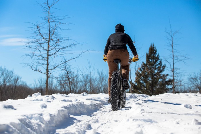 Rear view of a cyclist, riding Surly fat bike down a snow covered trail, with a trees ahead of them
