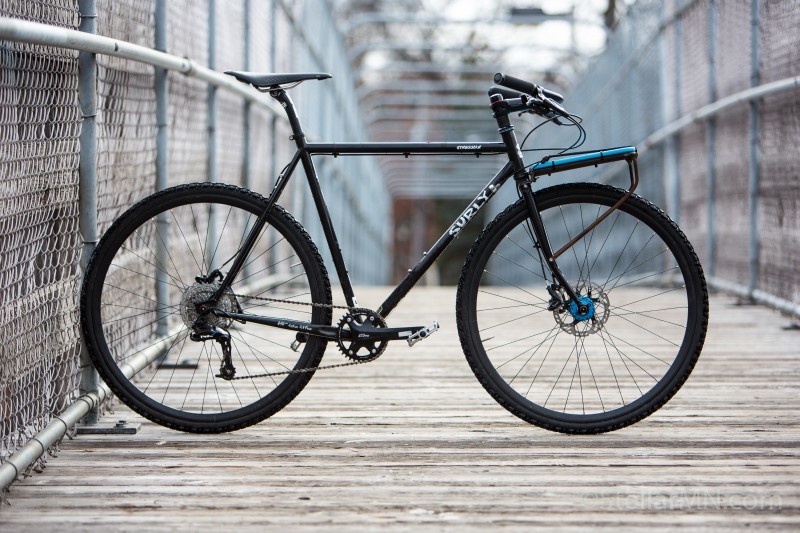 Right profile of a Surly Straggler bike, black, standing across a wood deck bridge with chain link on the sides