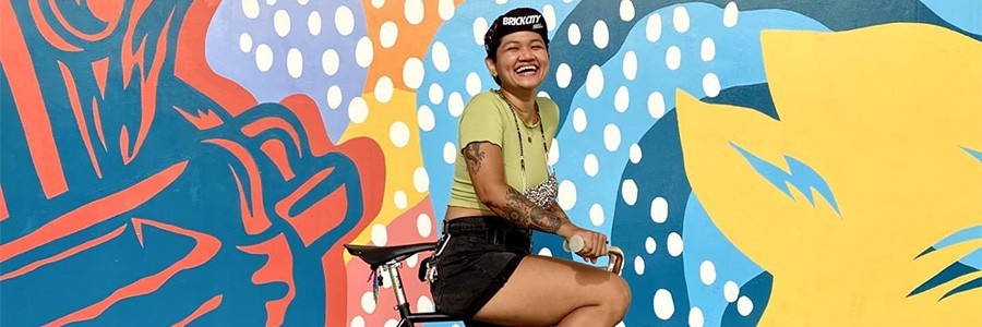 Aneka on Surly Steamroller bike with one foot down, smiling, in front of mural