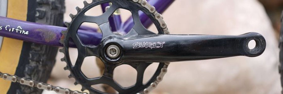 Close up of a black Surly crankset with a portion of the chain and rear tire on a purple Surly Pugsley fat bike