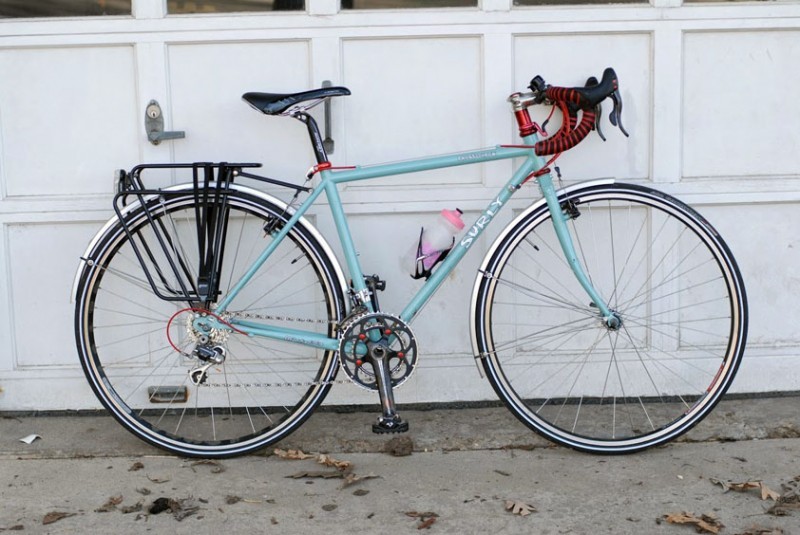 Right side view of a mint Surly Cross Check bike, leaning on the outside of a white garage door