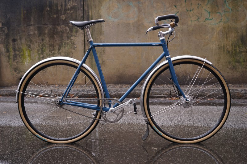 Right profile of a blue Surly bike, standing in water of a paved street
