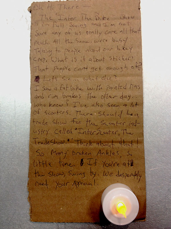 Downward view of a letter, written on a rectangular piece of cardboard, with an LED candle at the bottom