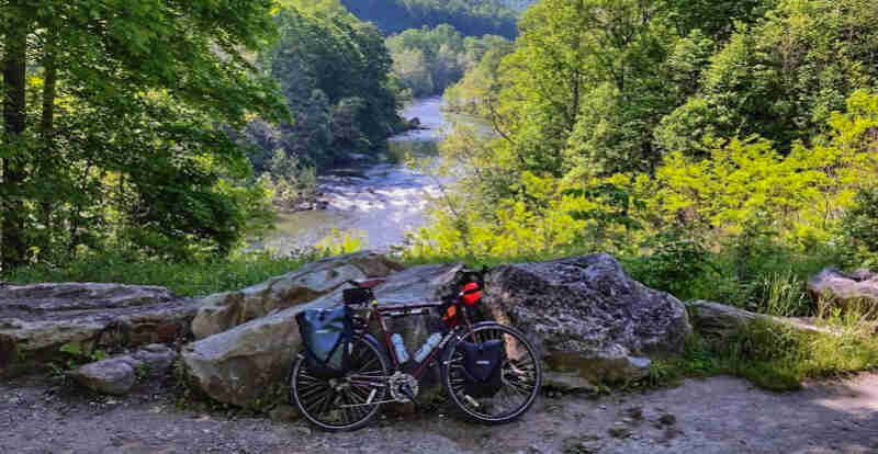 Right side view of a red Surly bike, loaded with gear, parked against a rock, with trees and a river in the background