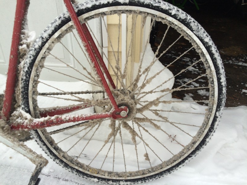 Left side view of the back end of red bike with snow and ice coating the rear wheel