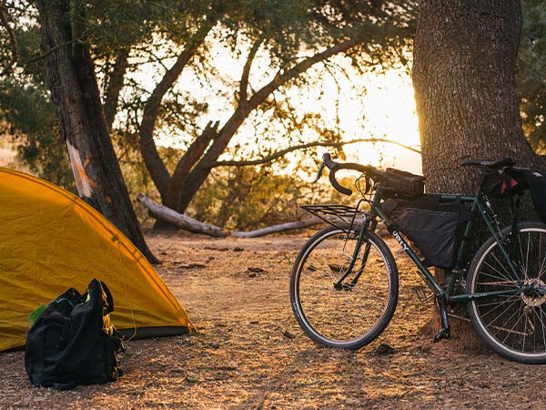 Drop bar bike with frame pack and bag parked against tree at camp, tent set-up