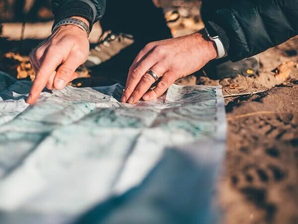 Close-up of person looking at folding map laid out on dirt in sun
