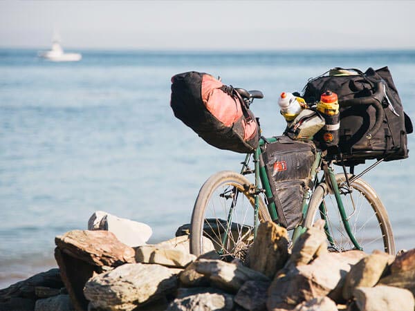 Surly Pack Rat loaded with bags and framepack on rocky shoreline, boat in distance