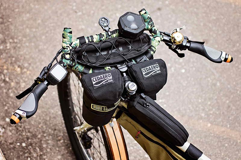 Downward close up view of a Surly Big Easy bike handlebar loaded with black gear packs and wooden fender and front wheel