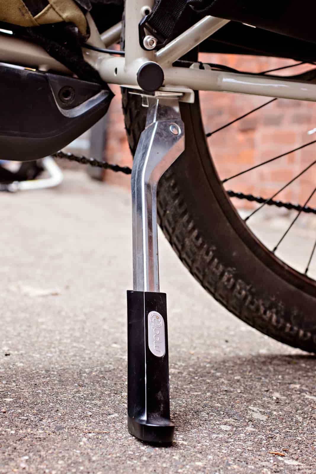 Close up of a kickstand mounted to a bike in the down position on top of pavement 