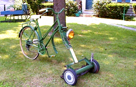 Front, right side view of a green bike, with a reel mower attached where the front wheel goes, on a front yard