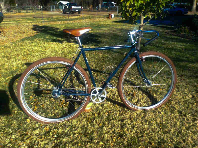 Right side view of a dark green Surly bike with a brown seat and tires, parked in a grass field
