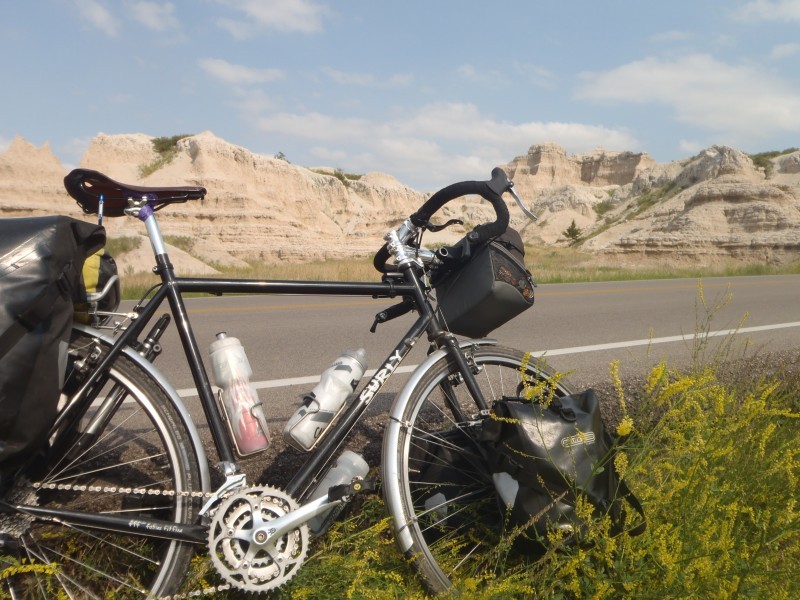 Right side view of a black Surly bike, parked in yellow brush on a roadside, with hills in the background
