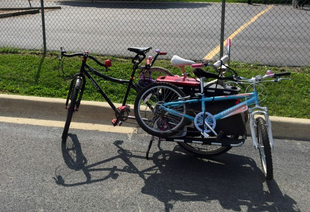Left side view of a Surly bike with 2 bikes on back, on the side of a street, with a parking lot in the background
