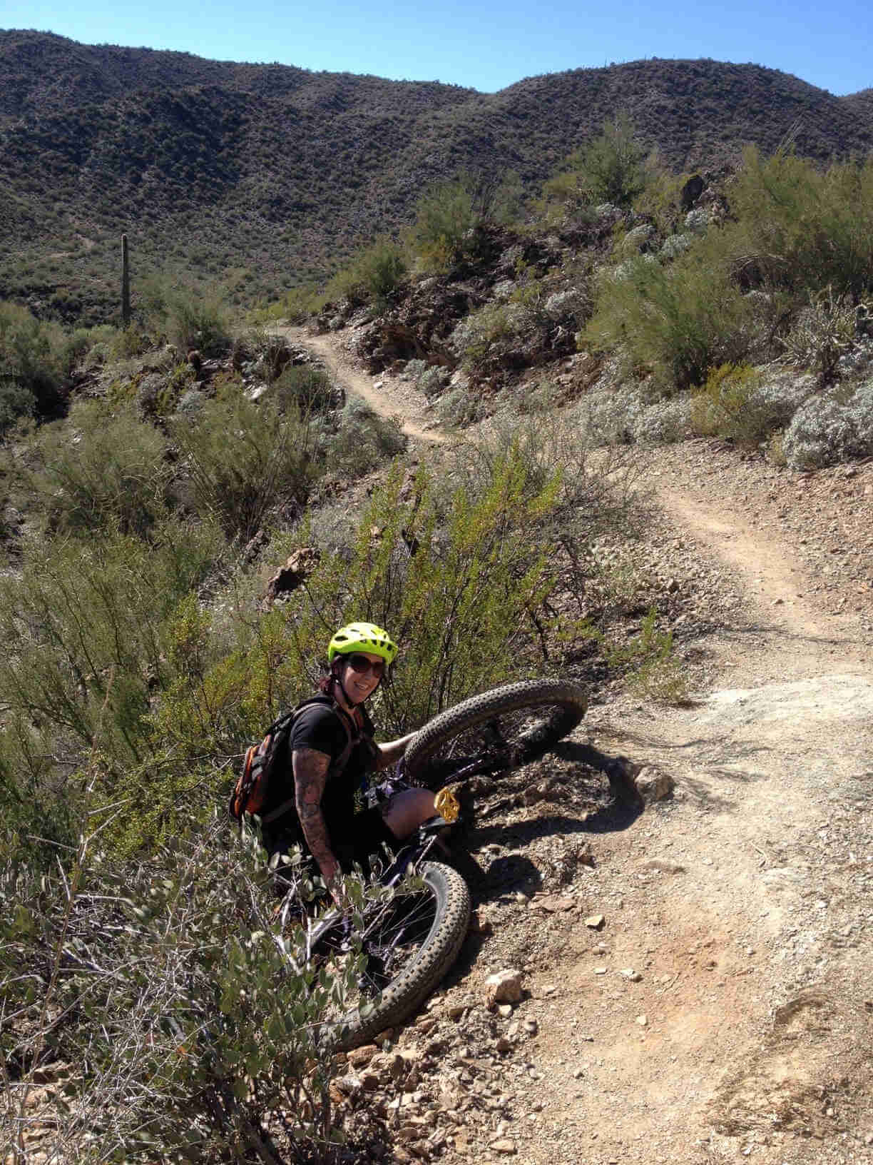 Rear view of a cyclist and their fat bike, laying in the brush on the side of a dirt trail in the desert hills