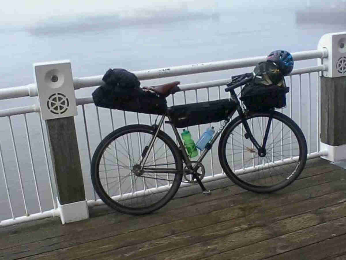 Right side view of a silver Surly bike, loaded with gear, parked against a railing, with a foggy background