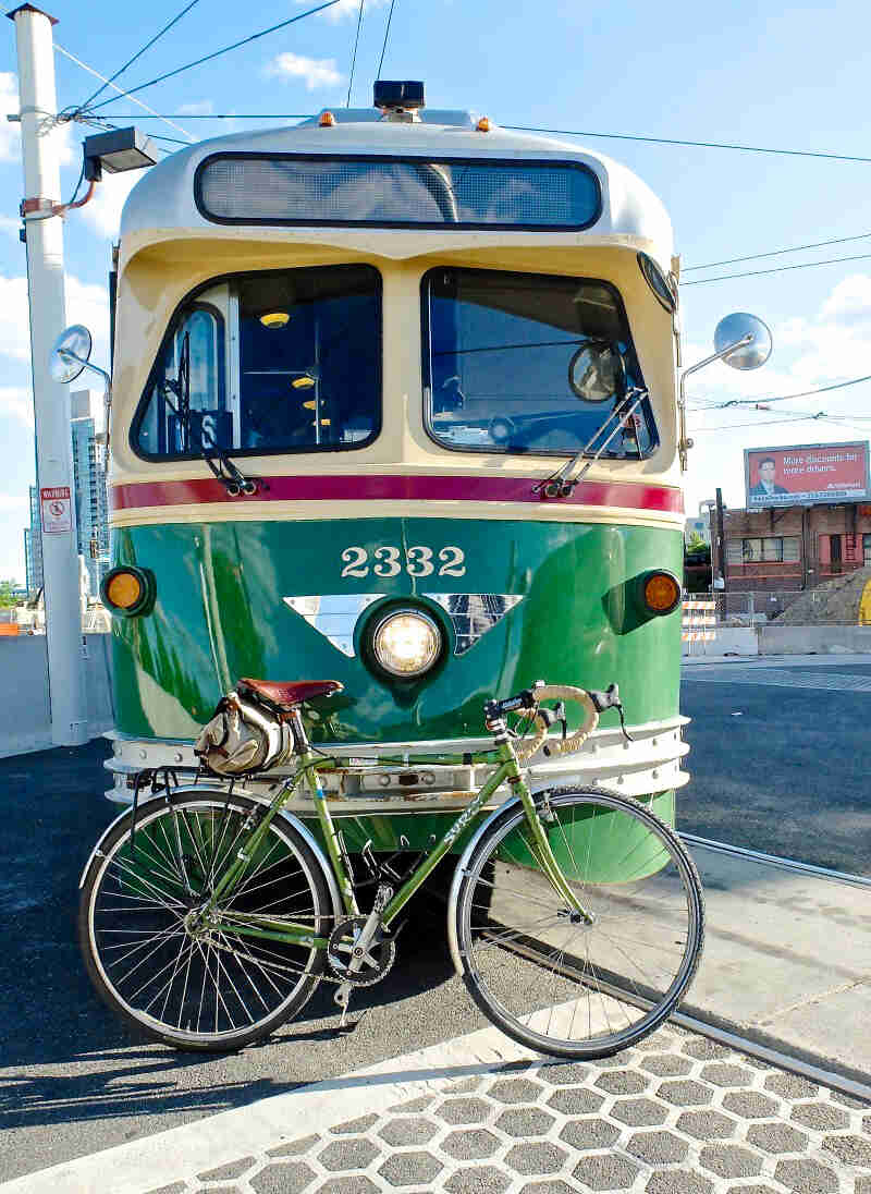 Right side view of a green Surly Cross Check bike, parked against the front of a street trolley