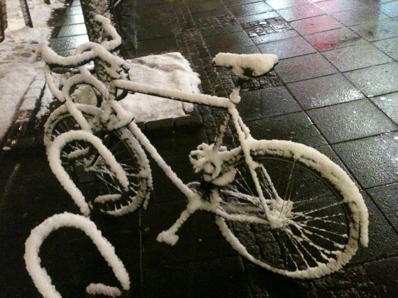 Right side view of a Surly Cross Check bike, covered in snow, parked in a bike rack on a sidewalk