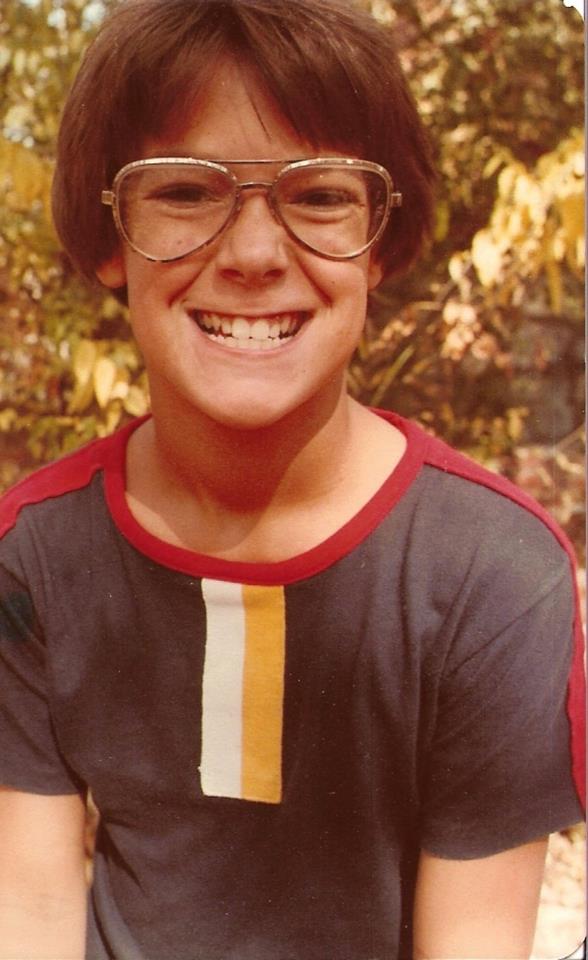 Front view of a child with glasses, from the waist up, posing for a picture