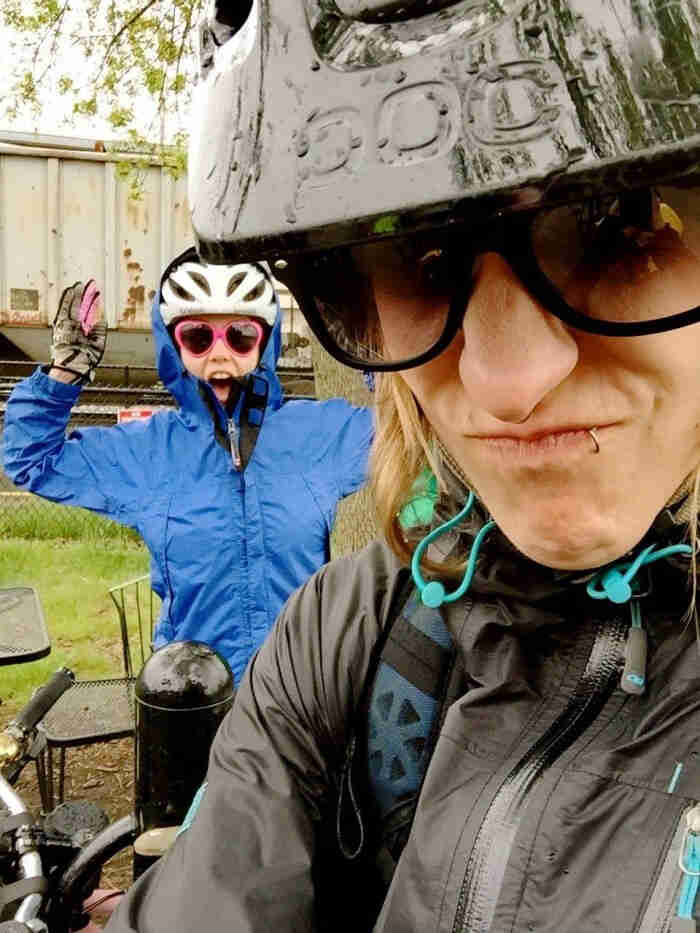 A closed up of a person, wearing a bike helmet, making an angry face, with another person standing behind them