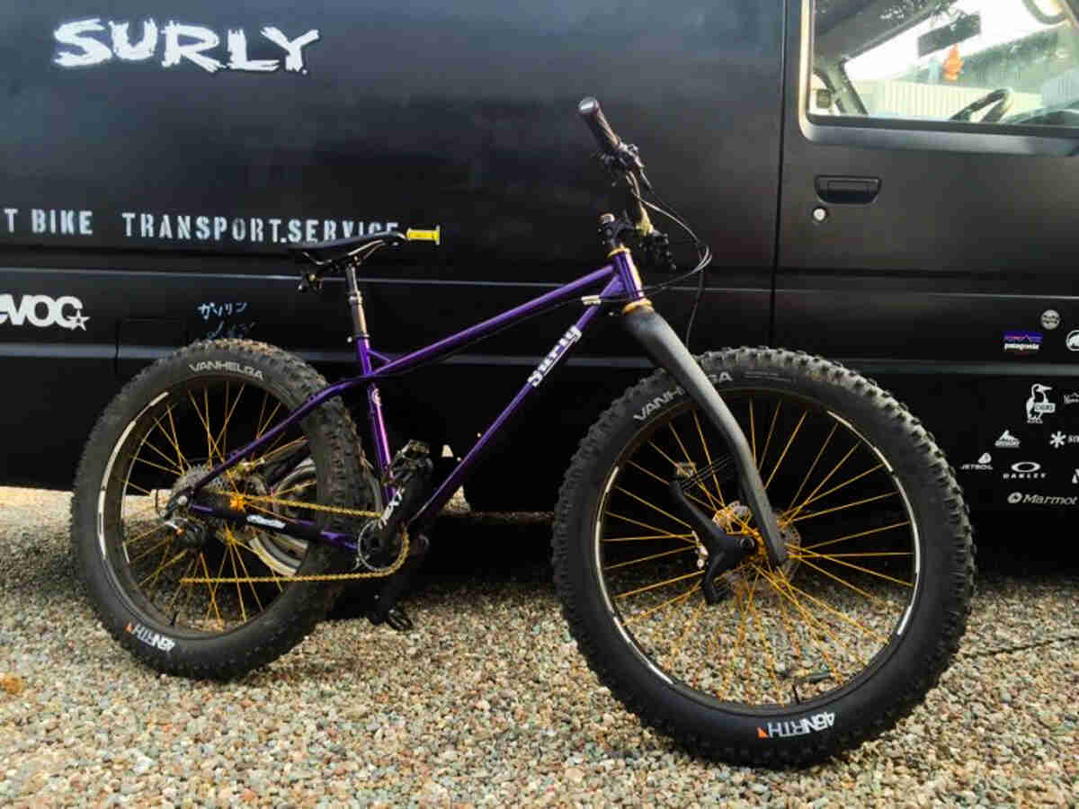 Right side view of a purple Surly fat bike, parked along the right side of a black van