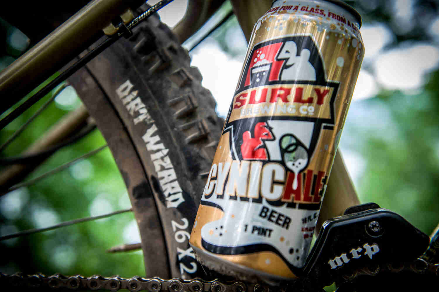 Close of view of a can of beer, sitting on the chain of a bike with a Surly Dirt Wizard tire on back