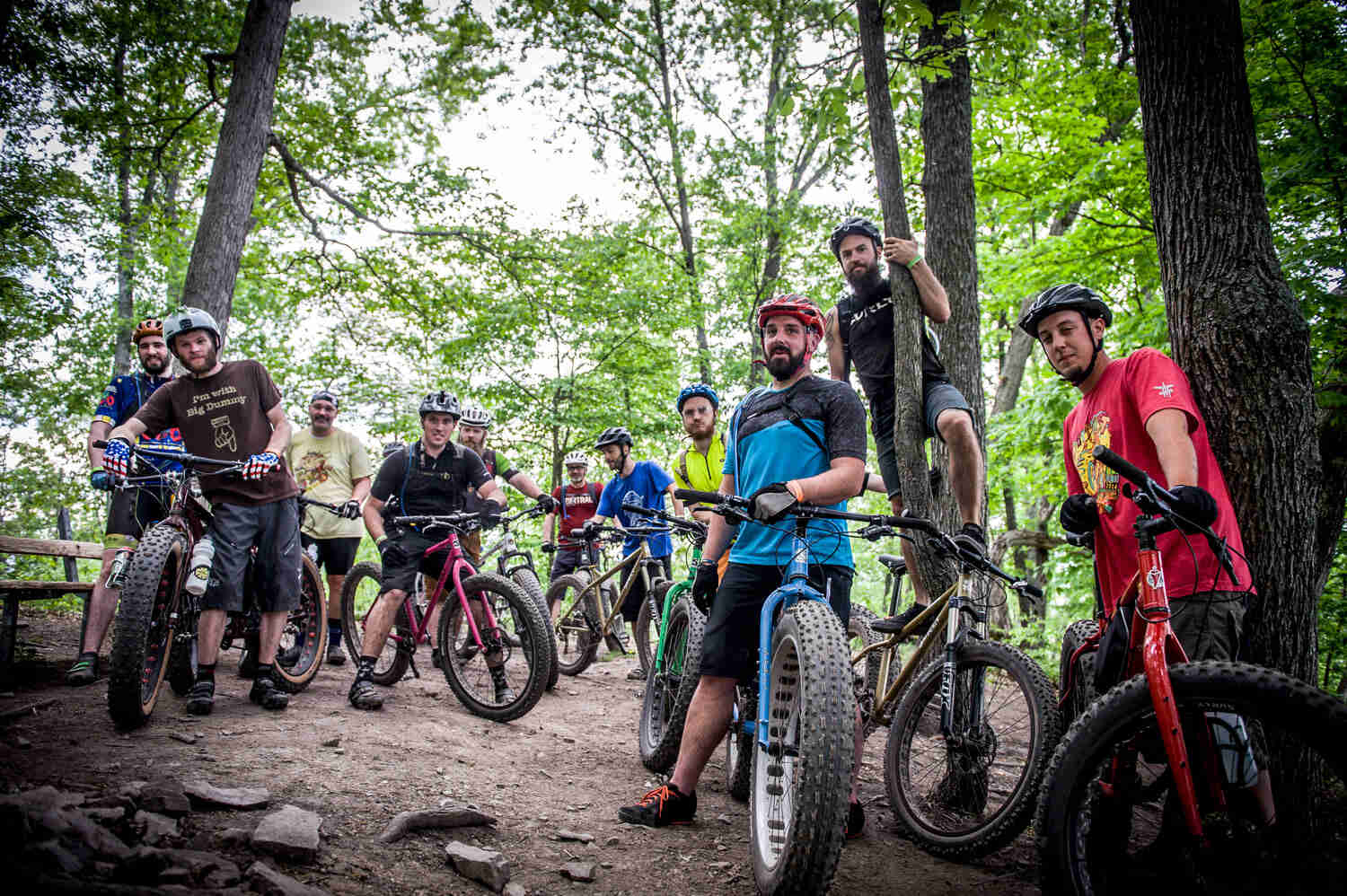 A group of cyclists, standing with their Surly fat bikes on a rocky dirt trail in a forest