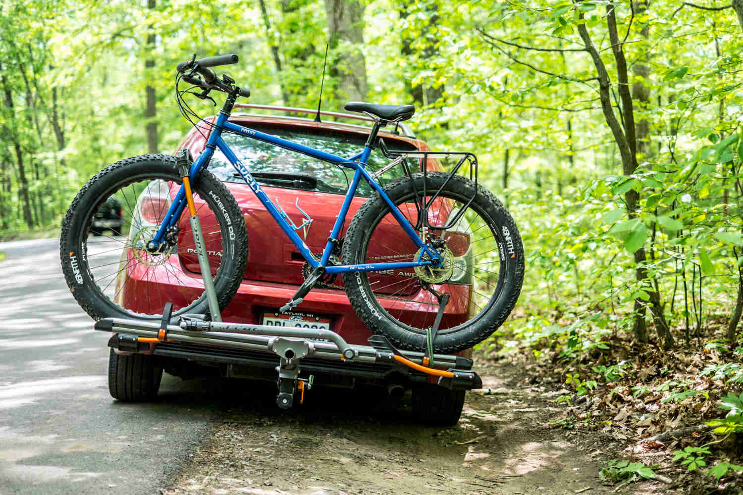Left side view of a blue Surly Pugsley fat bike, on a rack mounted to the back of a vehicle, on a roadside in the forest