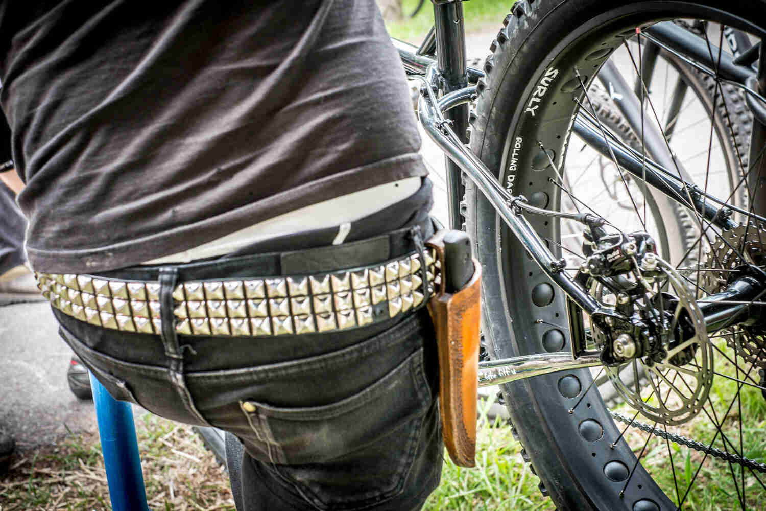 Rear view of a person's mid section, with a knife in a holster on a belt, and a Surly fat bike wheel on their right