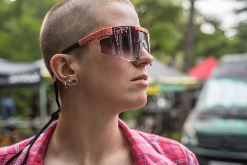 Right side profile of a person with a shaved head, wearing sunglasses, with a blurry background