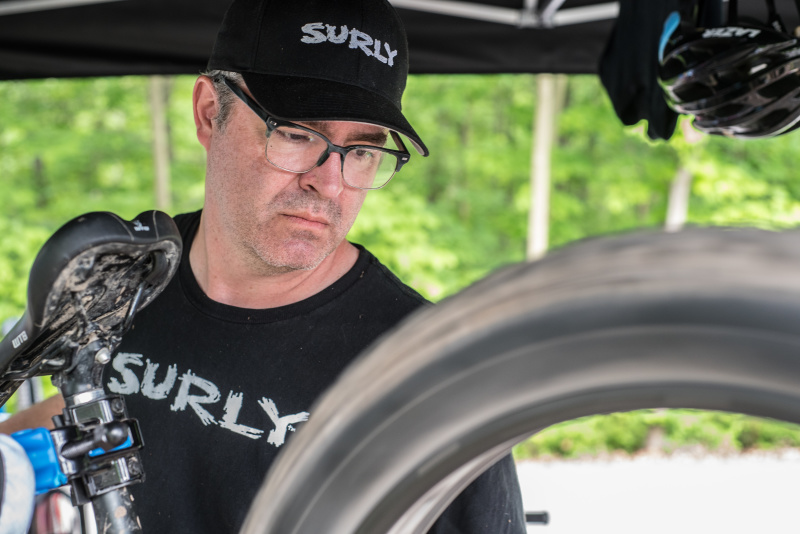 A person under a canopy, stares at a spinning rear fat bike tire, with trees in the background