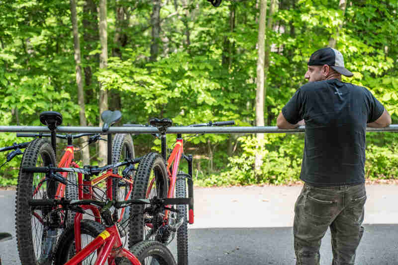 Rear view of a person next to bikes line up on a horizontal steel pole, with the forest in the background