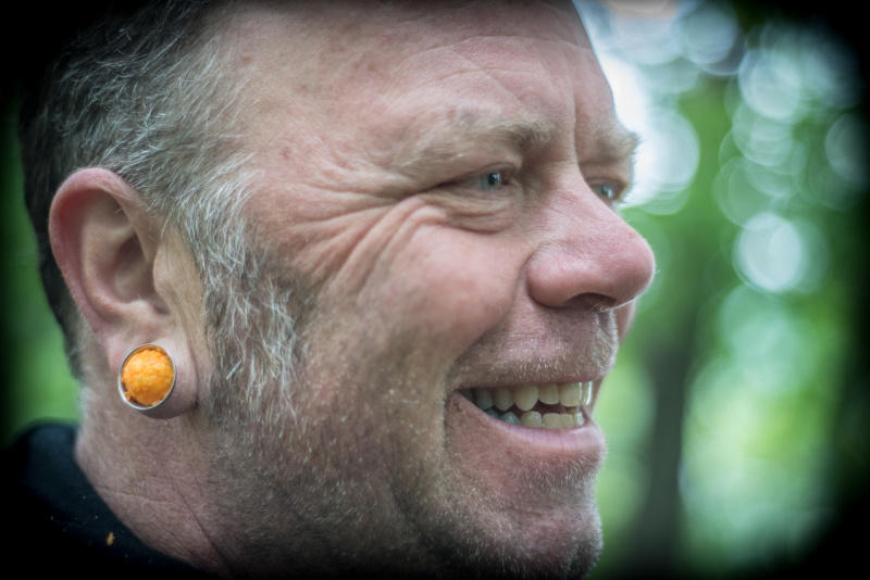 Right profile of a person smiling, with an orange, round object in their ear lobe 